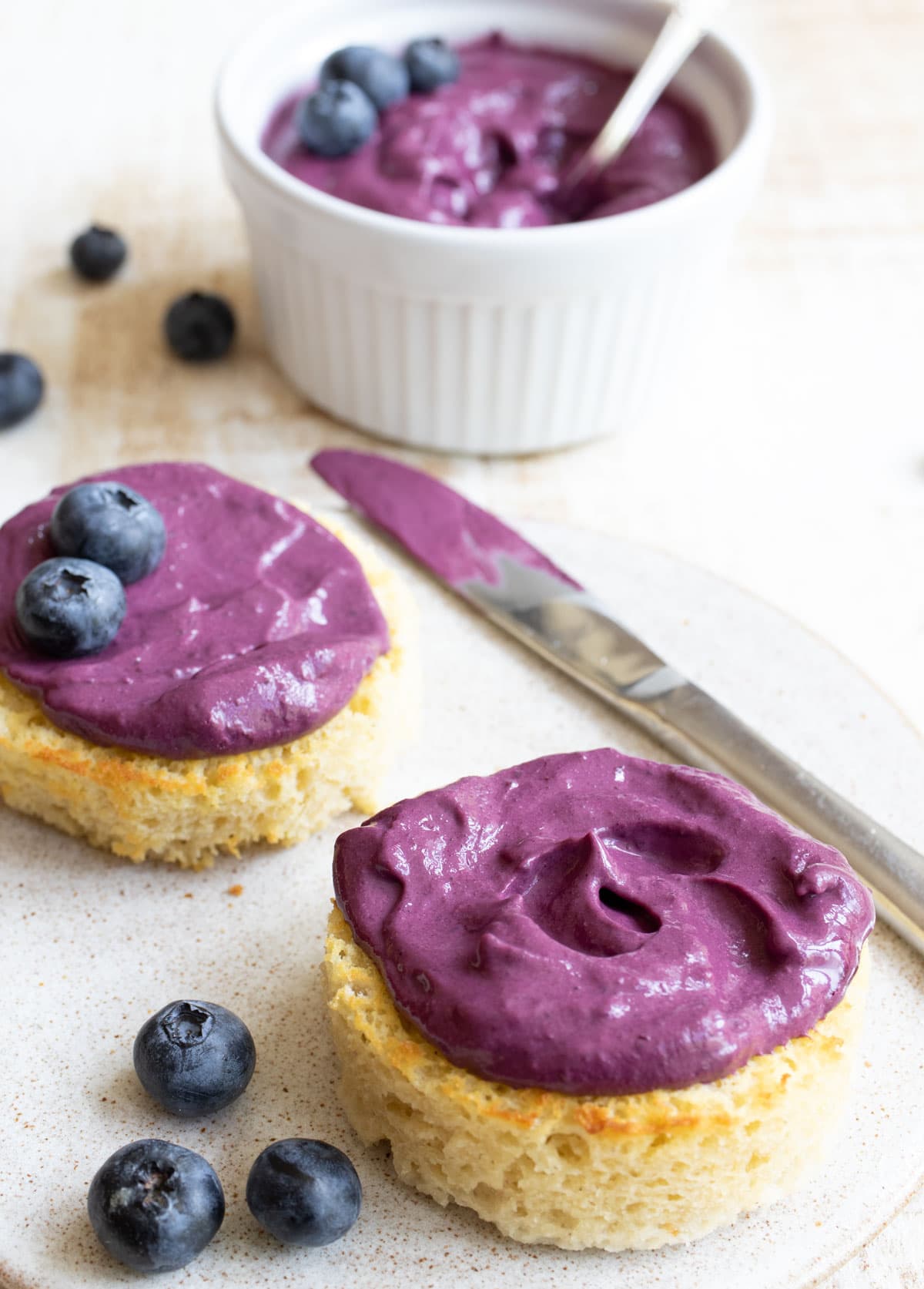 English muffins on a plate topped with blueberry cream cheese.