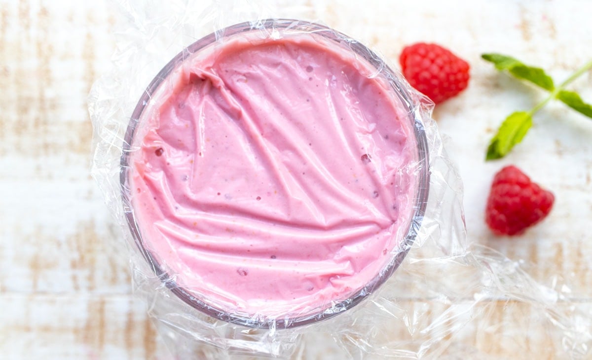 Covering up a glass of smoothie with clingfilm.