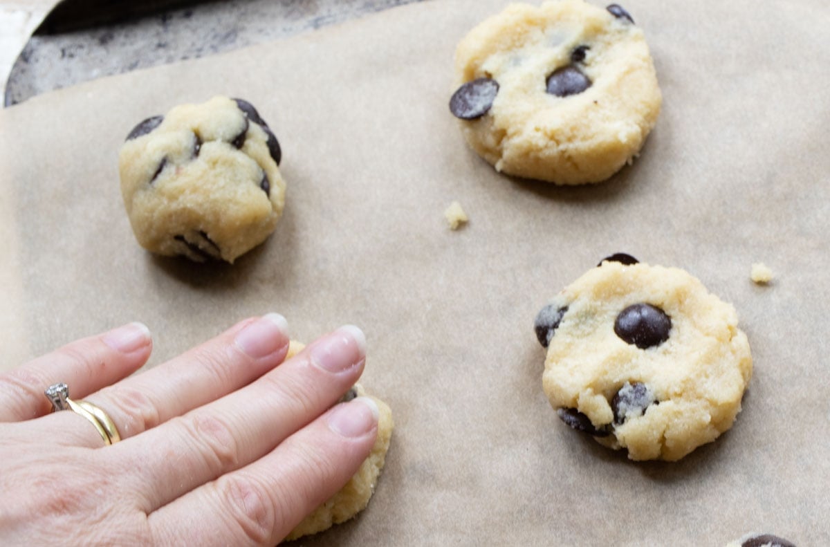 Hand pressing dough balls into cookie shapes on a cookie sheet lined with parchment paper.