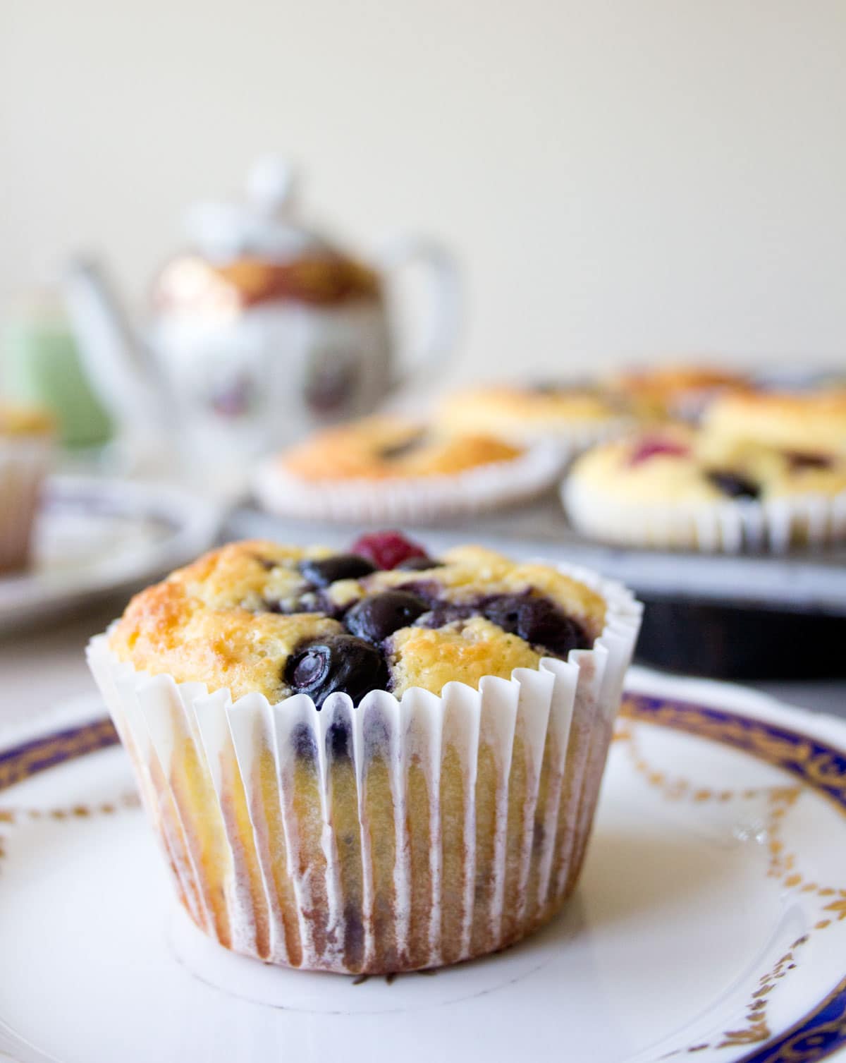Almond flour muffin with blueberries and raspberries in a paper muffin case on a plate.