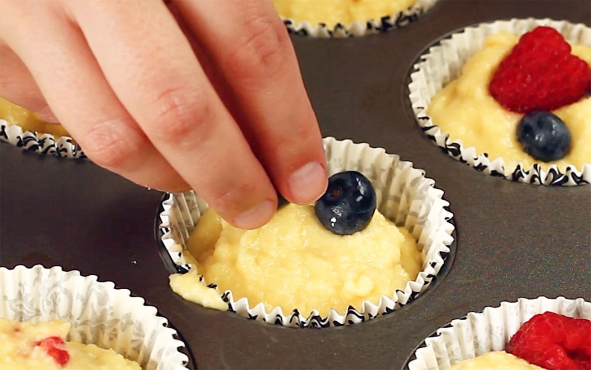 Adding blueberries on top of the muffin batter in the paper cup.