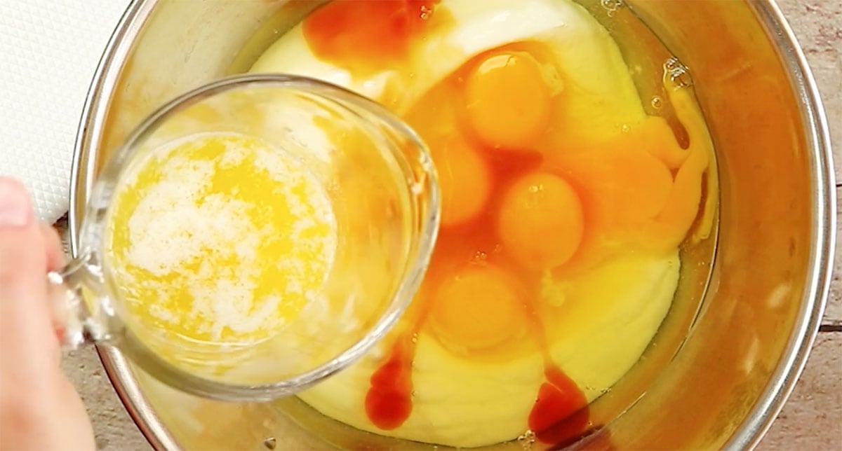 Pouring melted butter into a bowl with eggs, yogurt and vanilla extract.
