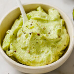 A bowl with avocado spread and a spoon.