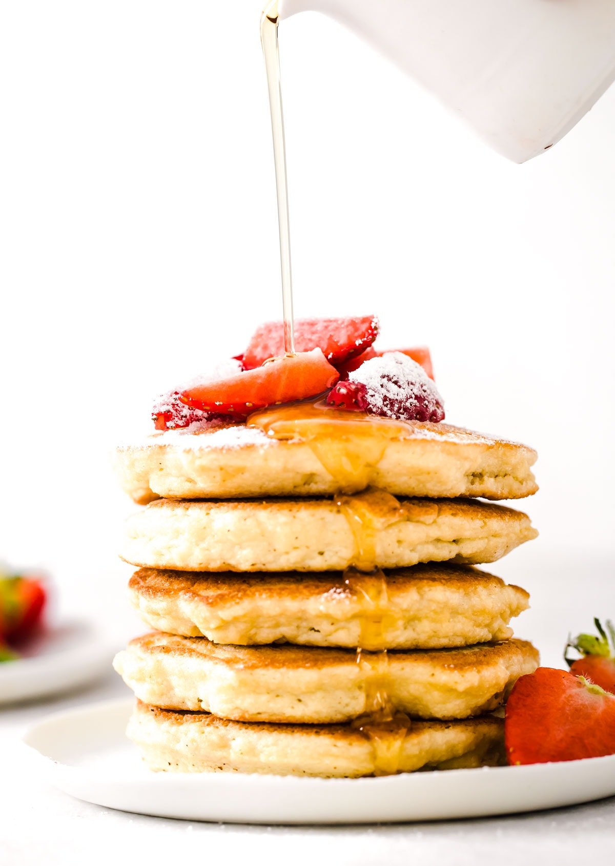 A stack of coconut flour pancakes topped with sliced strawberries and sugar free syrup.
