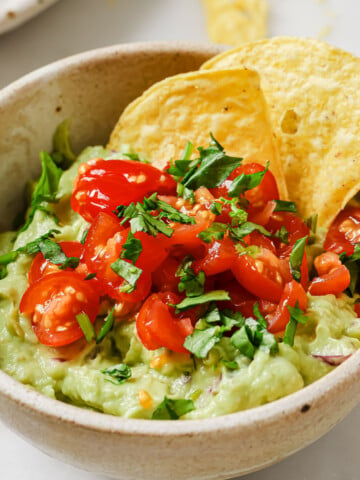 Guacamole in a bowl topped with sliced cherry tomatoes and tortilla chips.