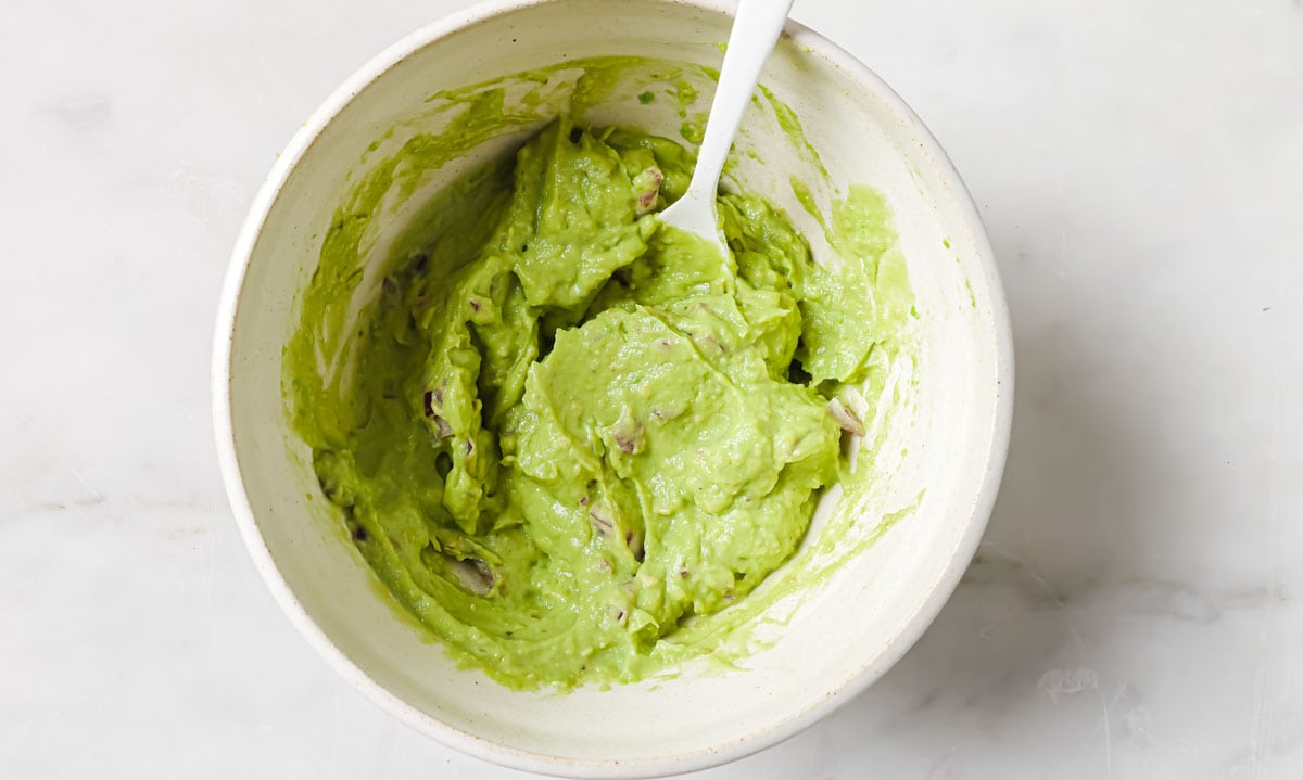 Creamed avocado and chopped red onions in a bowl with a spoon.