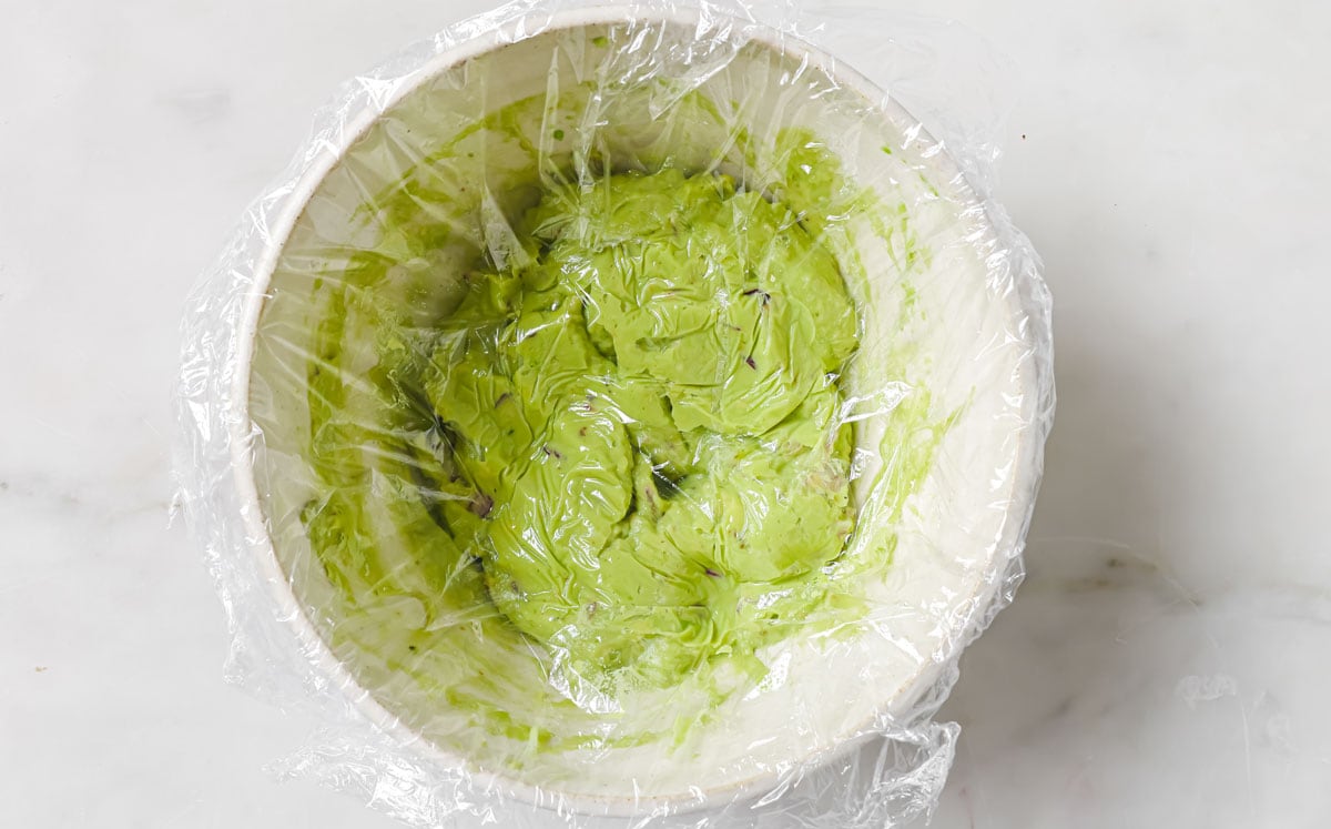 Tightly covering guacamole in a bowl with clingfilm, leaving no air pockets.