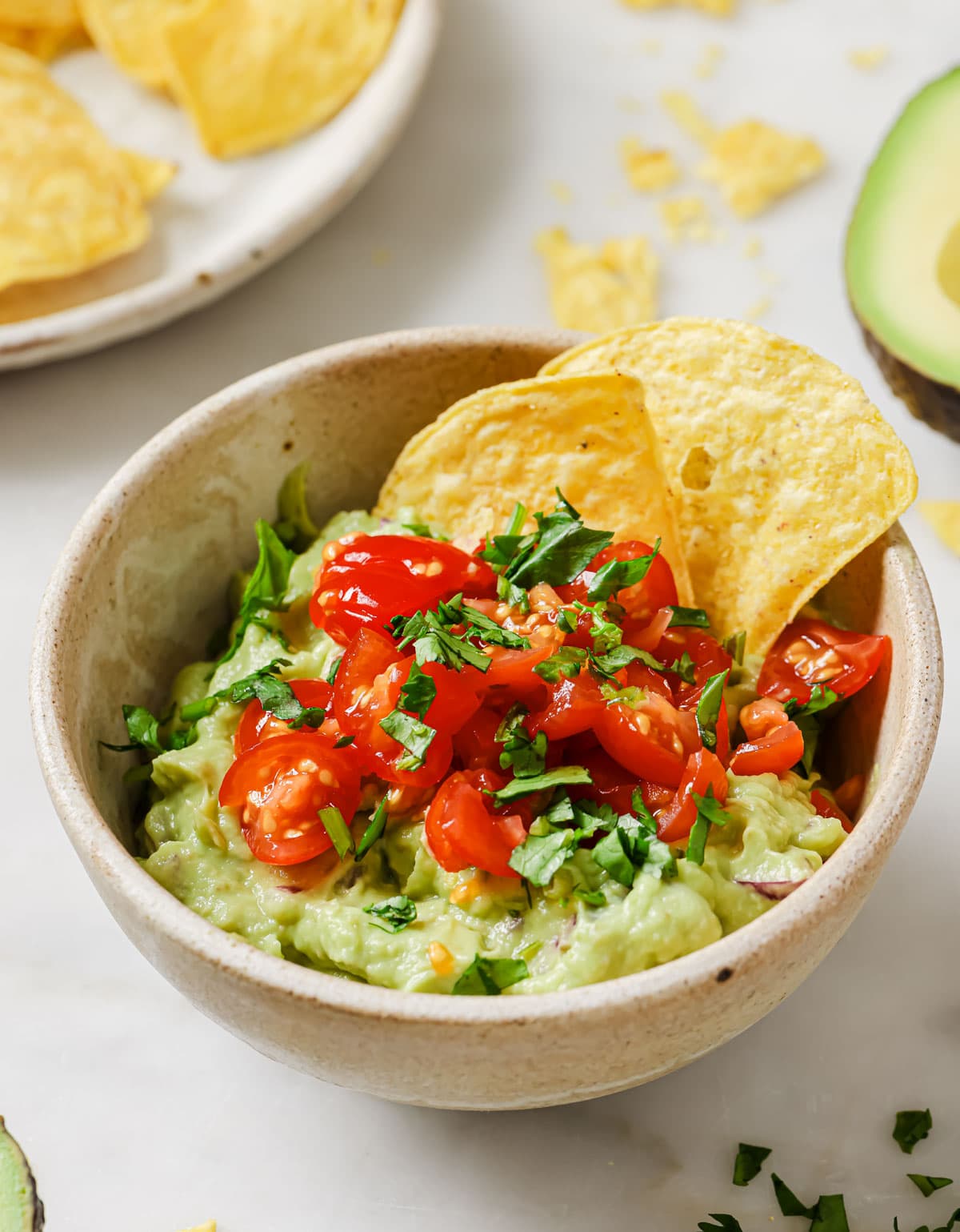 A bowl with 4 ingredient guacamole topped with halved cherry tomatoes and tortilla chips.