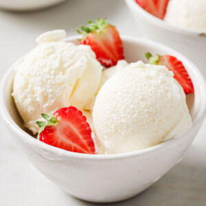 Frozen yogurt scoops in a bowl with halved strawberries.
