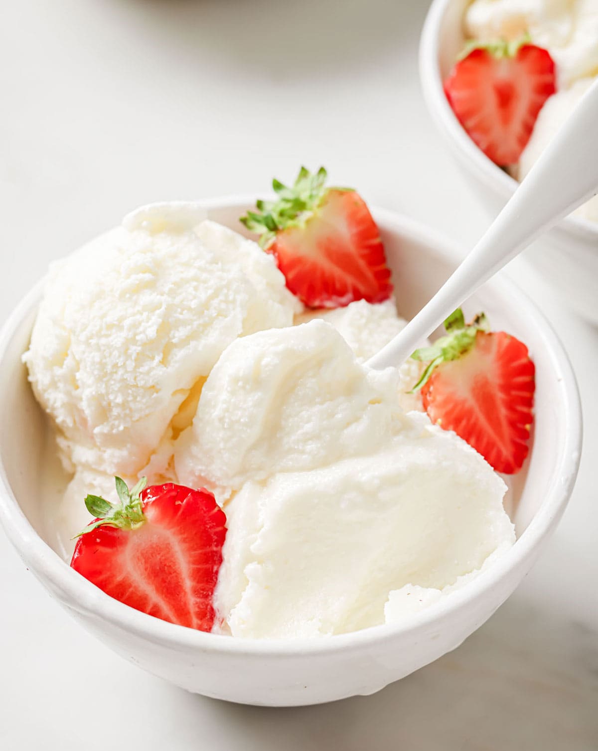 A bowl with frozen yogurt scoops, a spoon and strawberries.