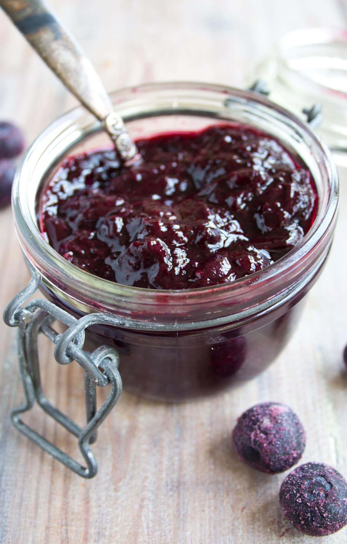 Sugar free blueberry jam in a glass jar with a spoon and blueberries.