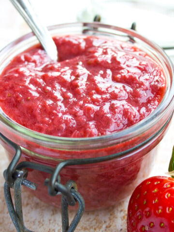 Sugar free strawberry jam in a glass jar with a spoon.