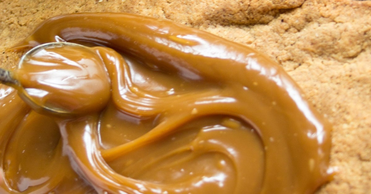 Spreading caramel over the baked crust with a spoon.