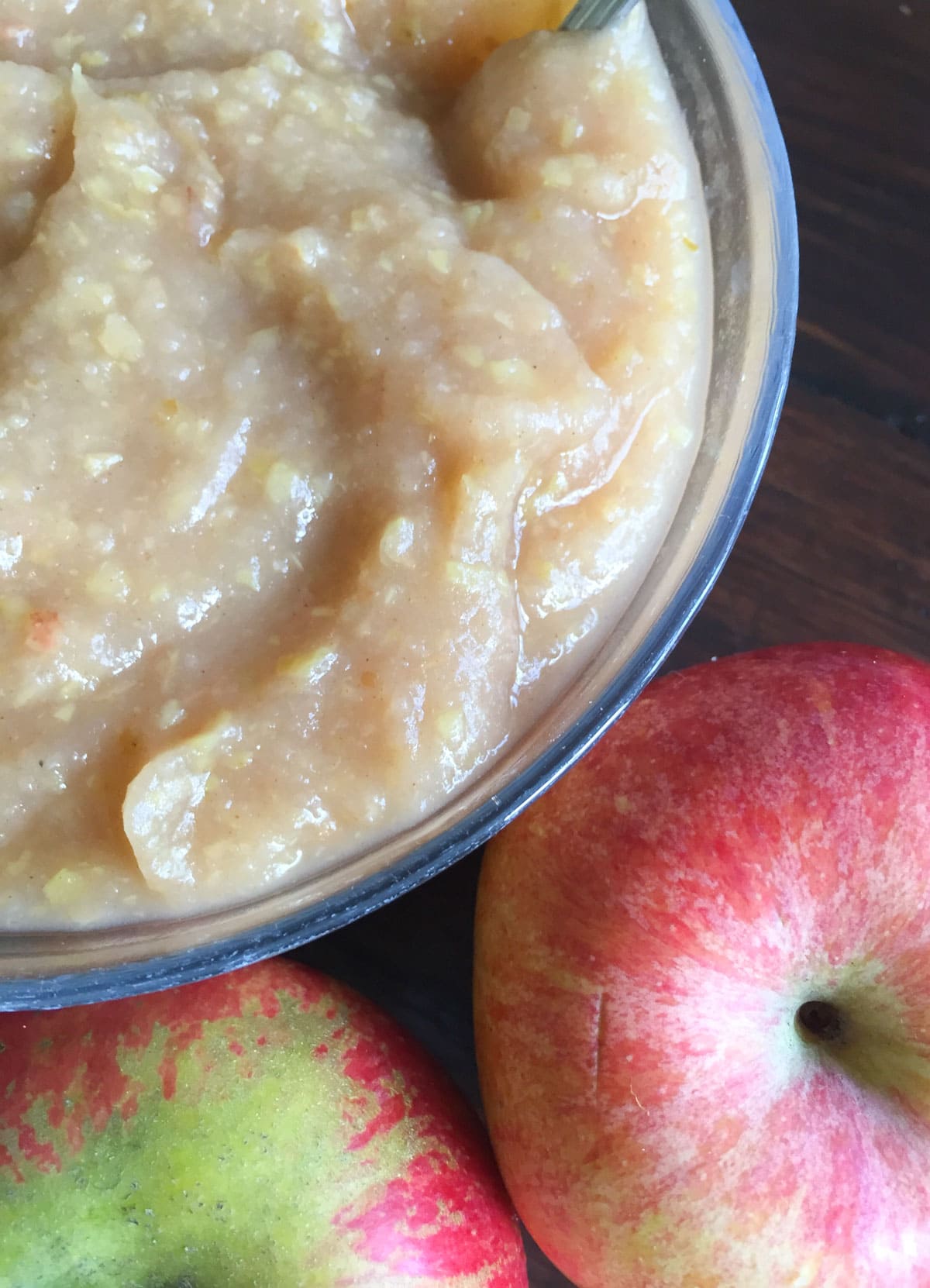 Unsweetened applesauce in a glass bowl with apples on the side.