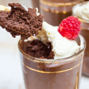 A spoonful of chocolate mousse and a cup with mousse topped with whipped cream and a raspberry.