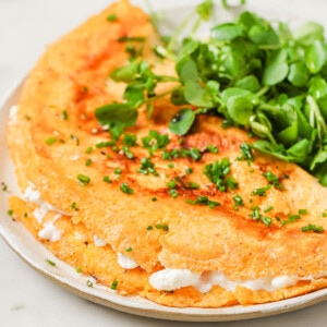 Cottage cheese omelette filled with cottage cheese on a plate with a side of green leaves.