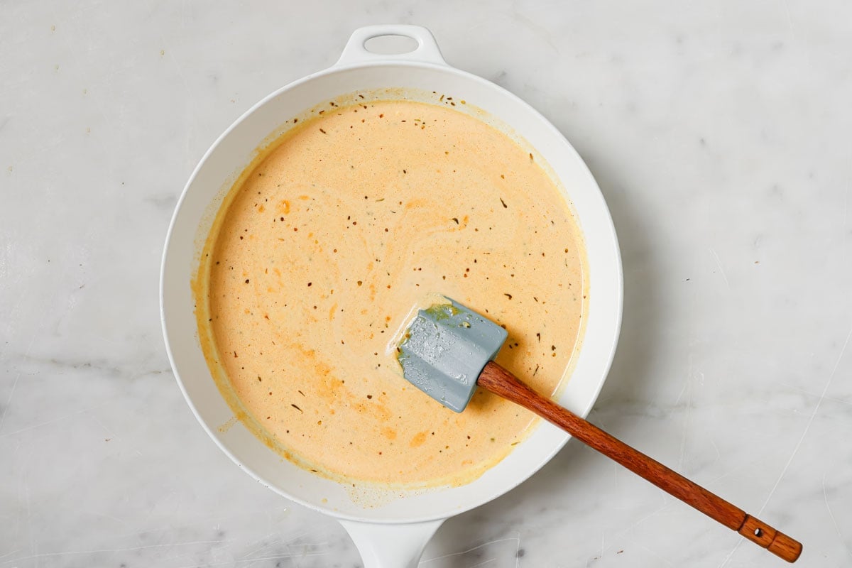 The cream sauce in the pan with parmesan, paprika and seasonings.