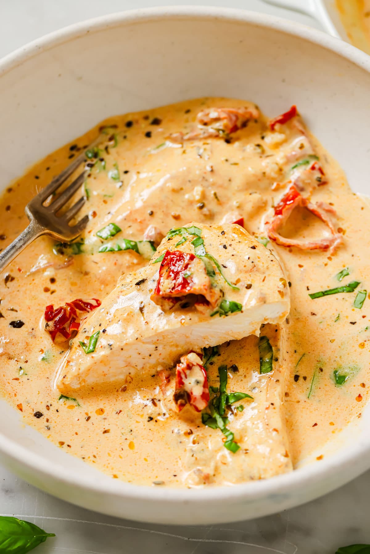 A sliced chicken fillet with marry me sauce, which is a creamy sauce with sun-dried tomatoes, in a bowl with a fork.