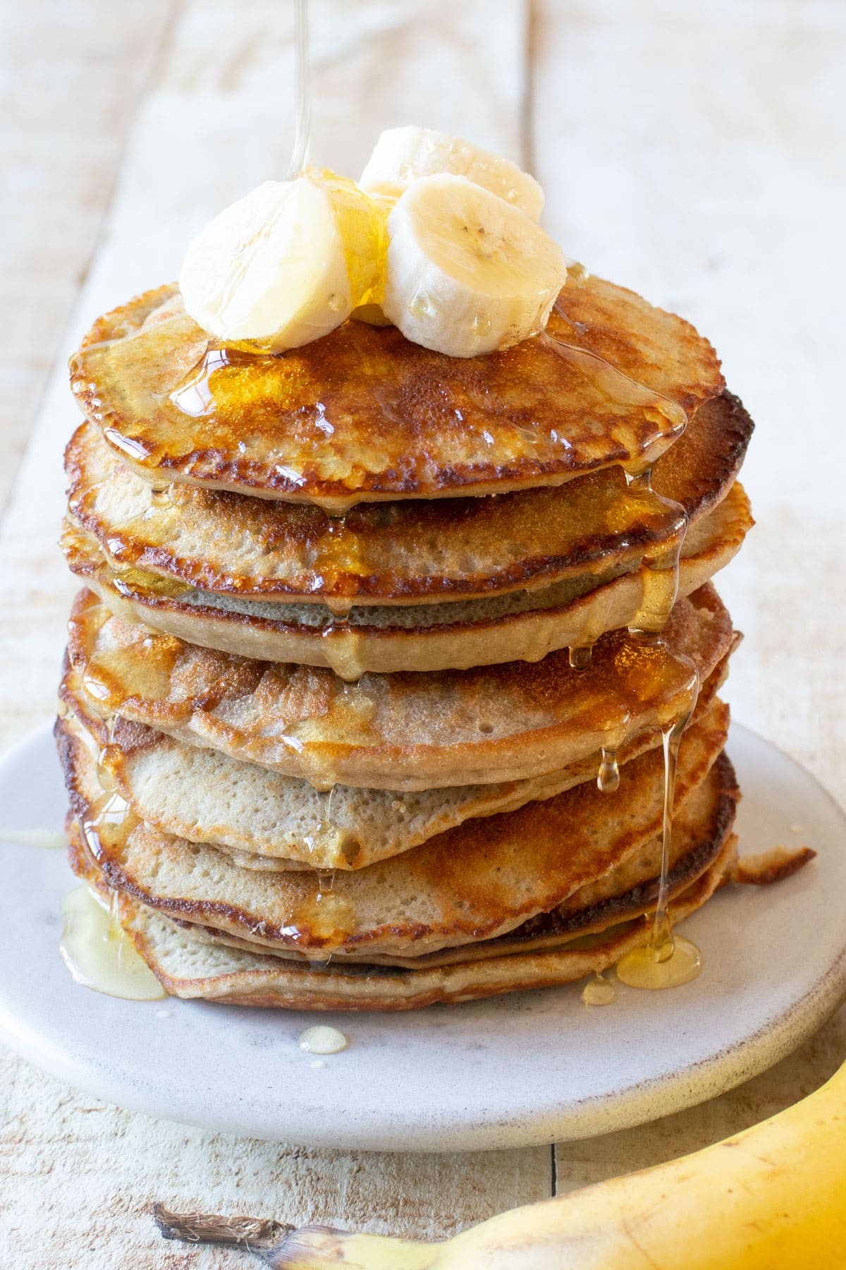 A stack of almond flour pancakes with banana slices on top and syrup.