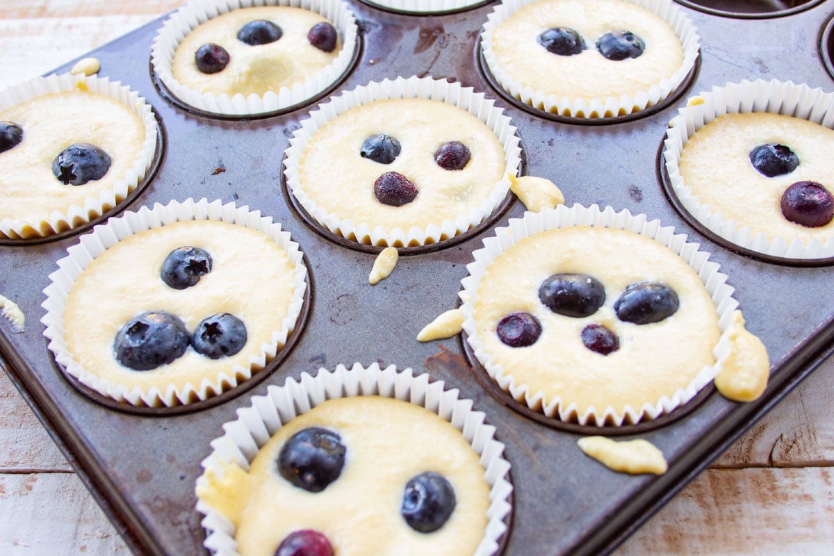 Muffin batter with blueberries in a muffin pan lined with paper cups.