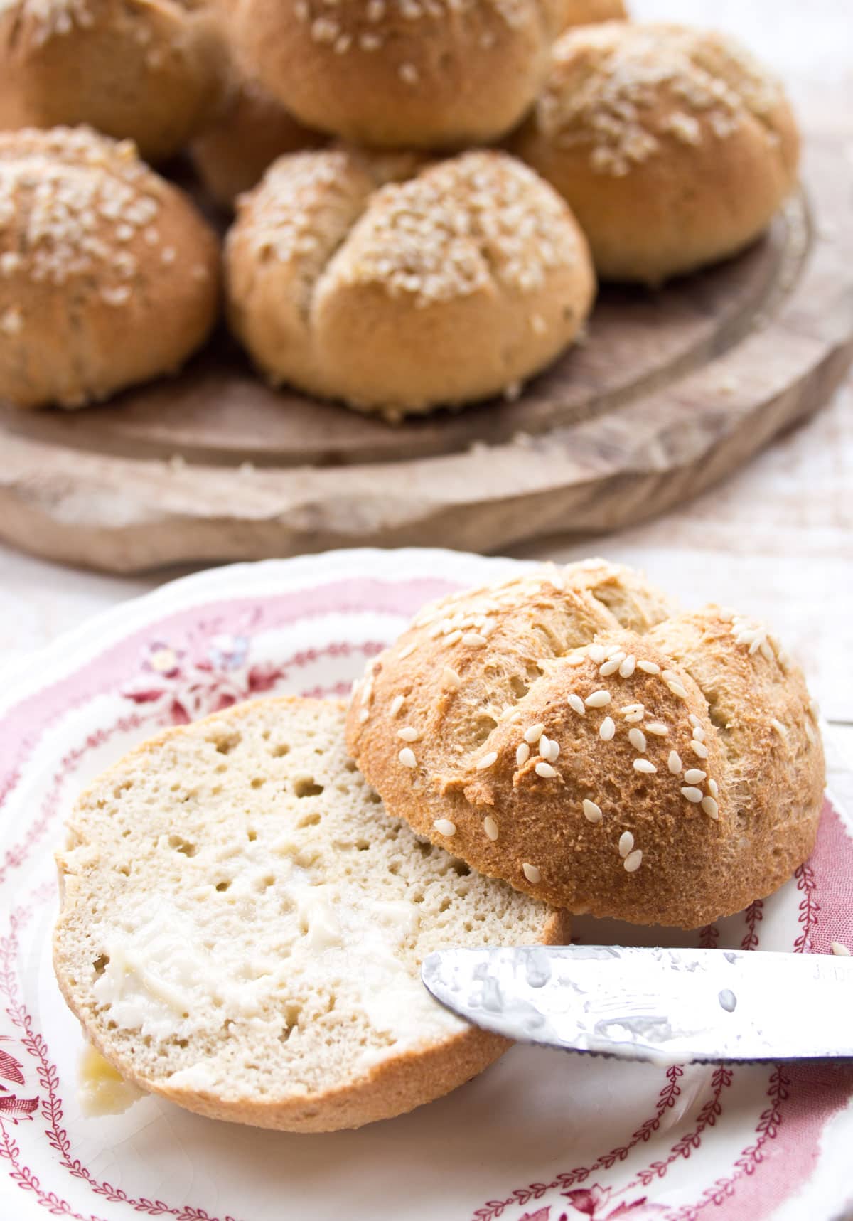 A sliced bun ith sesame seeds on a plate, spread with butter.