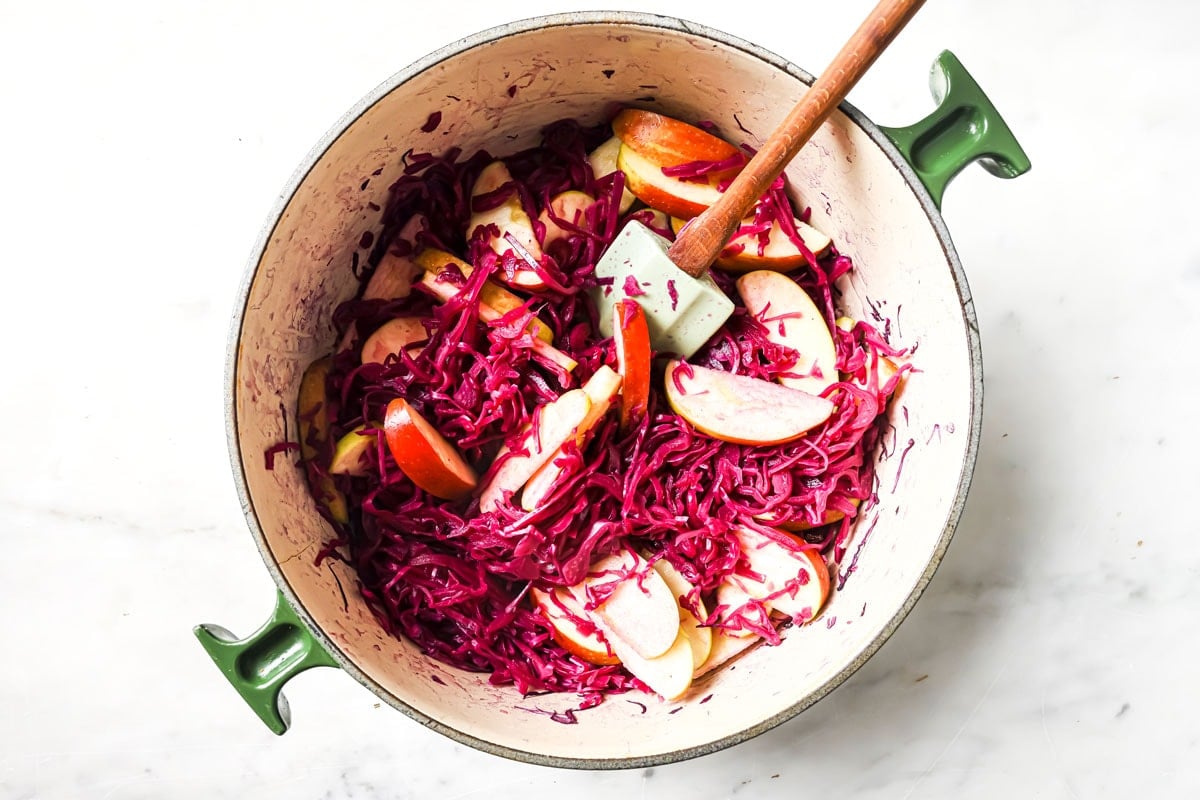 Cooked red cabbage with apple slices in a pot with a spatula.