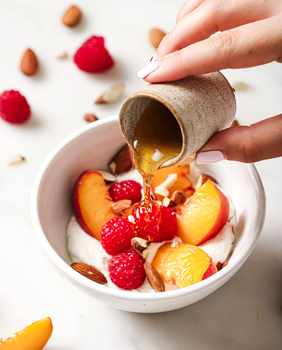 Pouring honey over a bowl with blended cottage cheese topped with peaches and raspberries.