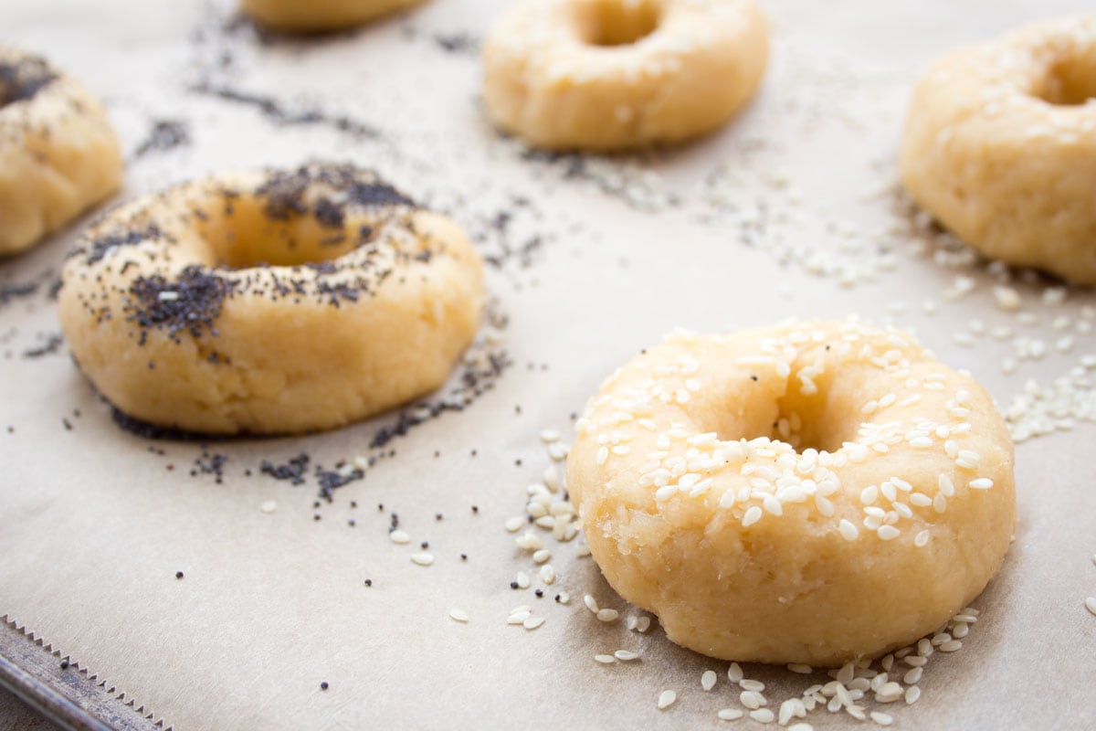 Unbaked bagels on a parchment paper lined baking tray.