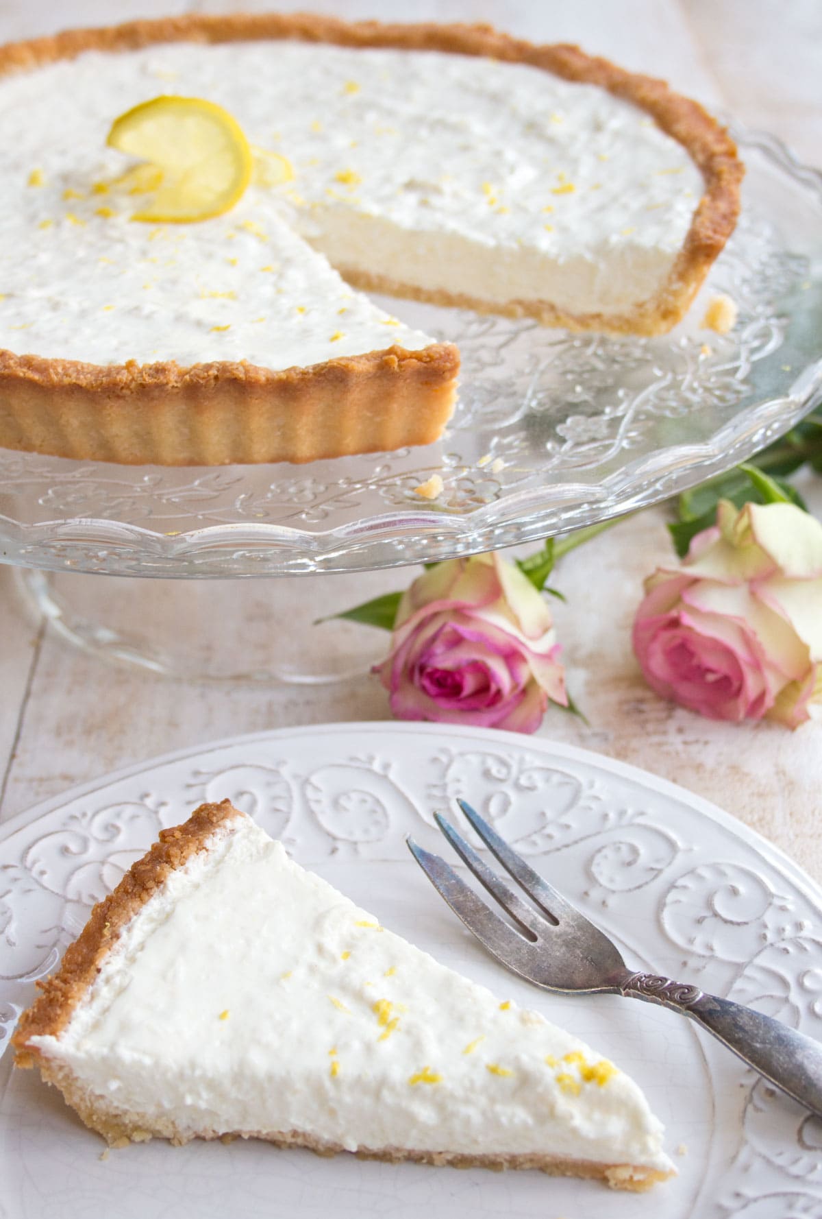 A lemon cheesecake on a cake stand and a slice of cake on a plate.