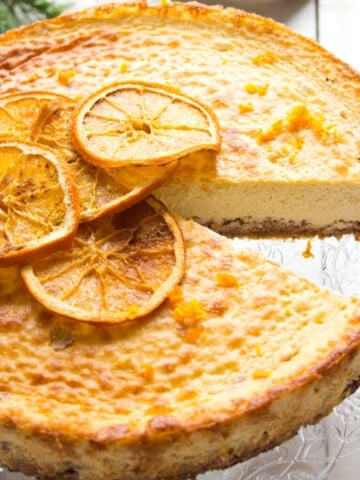 A baked orange cheesecake on a platter topped with dried orange slices.