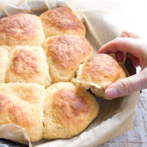 Pull-apart keto dinner rolls in a tray lined with parchment paper and a hand taking a roll.