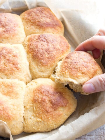 Pull-apart keto dinner rolls in a tray lined with parchment paper and a hand taking a roll.