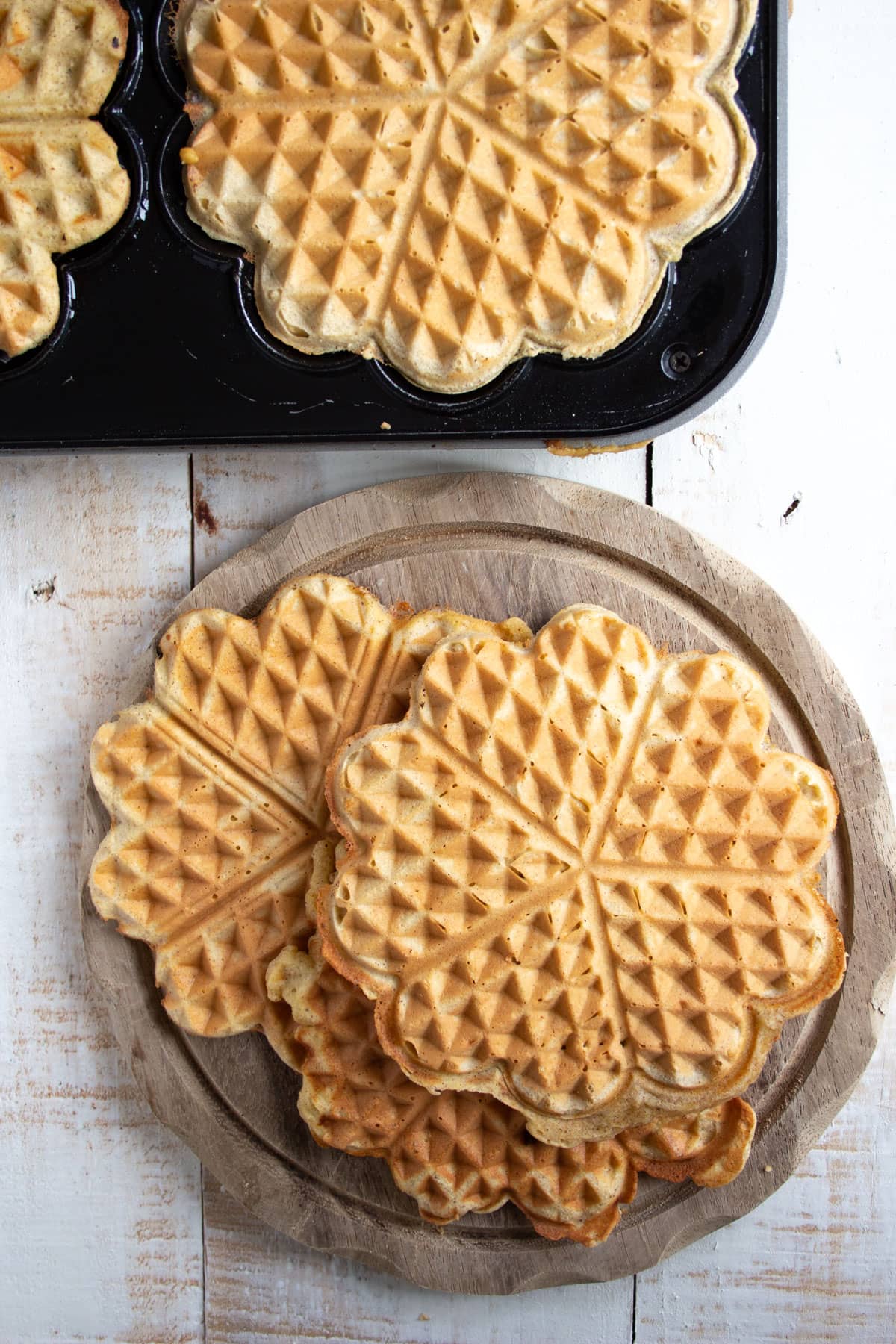 Waffles on a wooden board and waffles in a waffle maker.