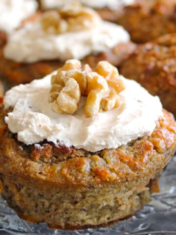 A diabetic carrot cake muffin topped with cream cheese frosting and a walnut.