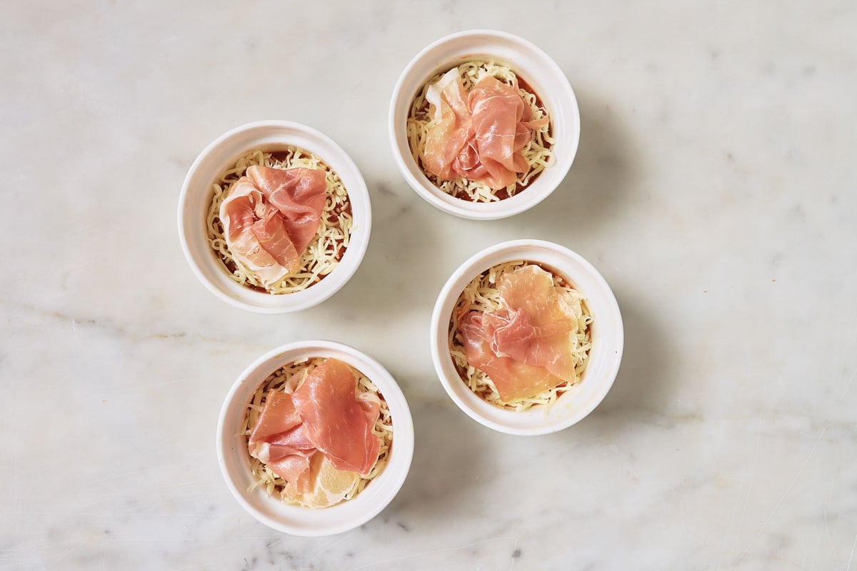 Adding cured ham on top of the pizz bowls.