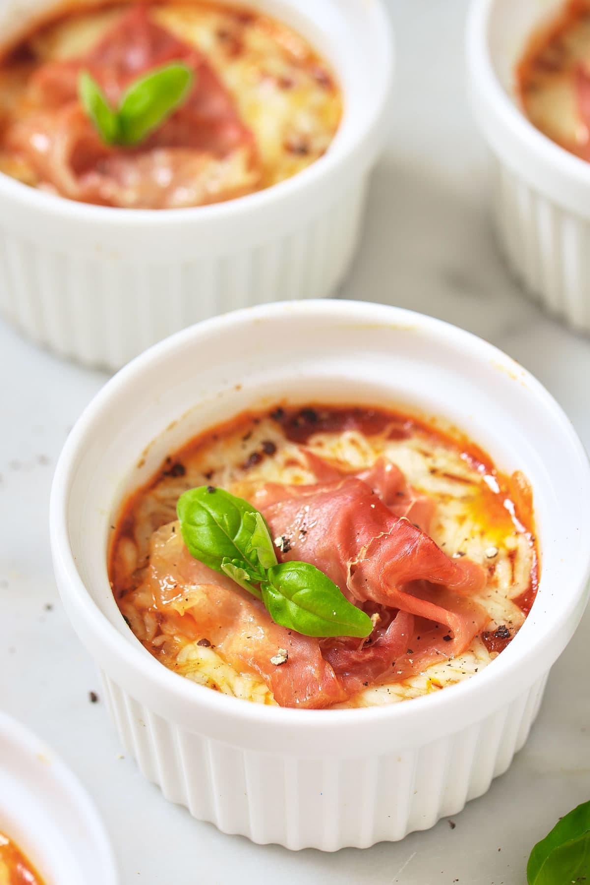 Pizza bowls topped with cured ham and basil leaf in ramekins.