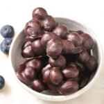 Chocolate covered blueberres in clusters in a bowl and fresh blueberries on the side.