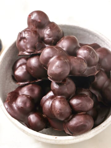 Chocolate covered blueberres in clusters in a bowl and fresh blueberries on the side.