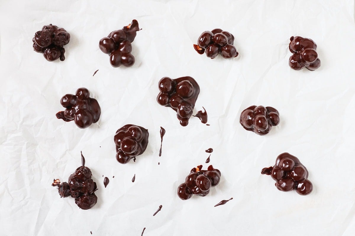 Cooling blueberry clusters covered in chocolate on parchment paper.