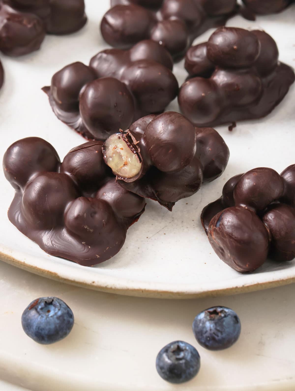 A chocolate coated blueberry cluster that is bitten into showing a blueberry inside.
