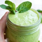 Hand holding a glass with a green smoothie decorated with a few mint leaves.