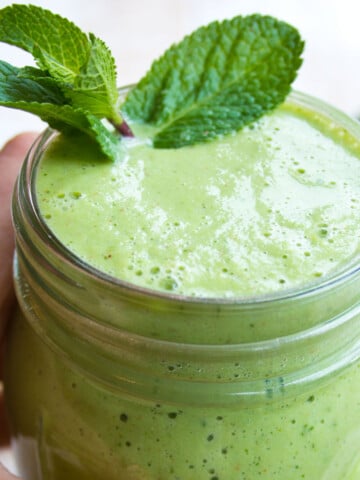 Hand holding a glass with a green smoothie decorated with a few mint leaves.