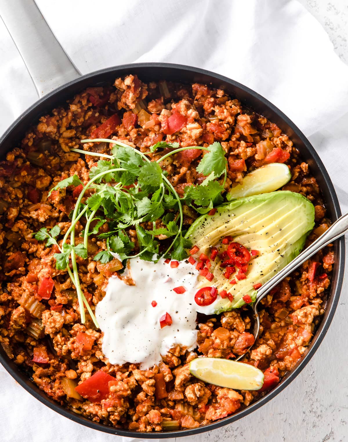 A pan with low carb chili, sour cream, avocado and cilantro.