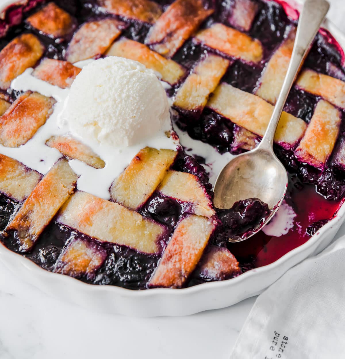A berry pie with a lattice crust topping and a scoop of vanilla ice cream on top.
