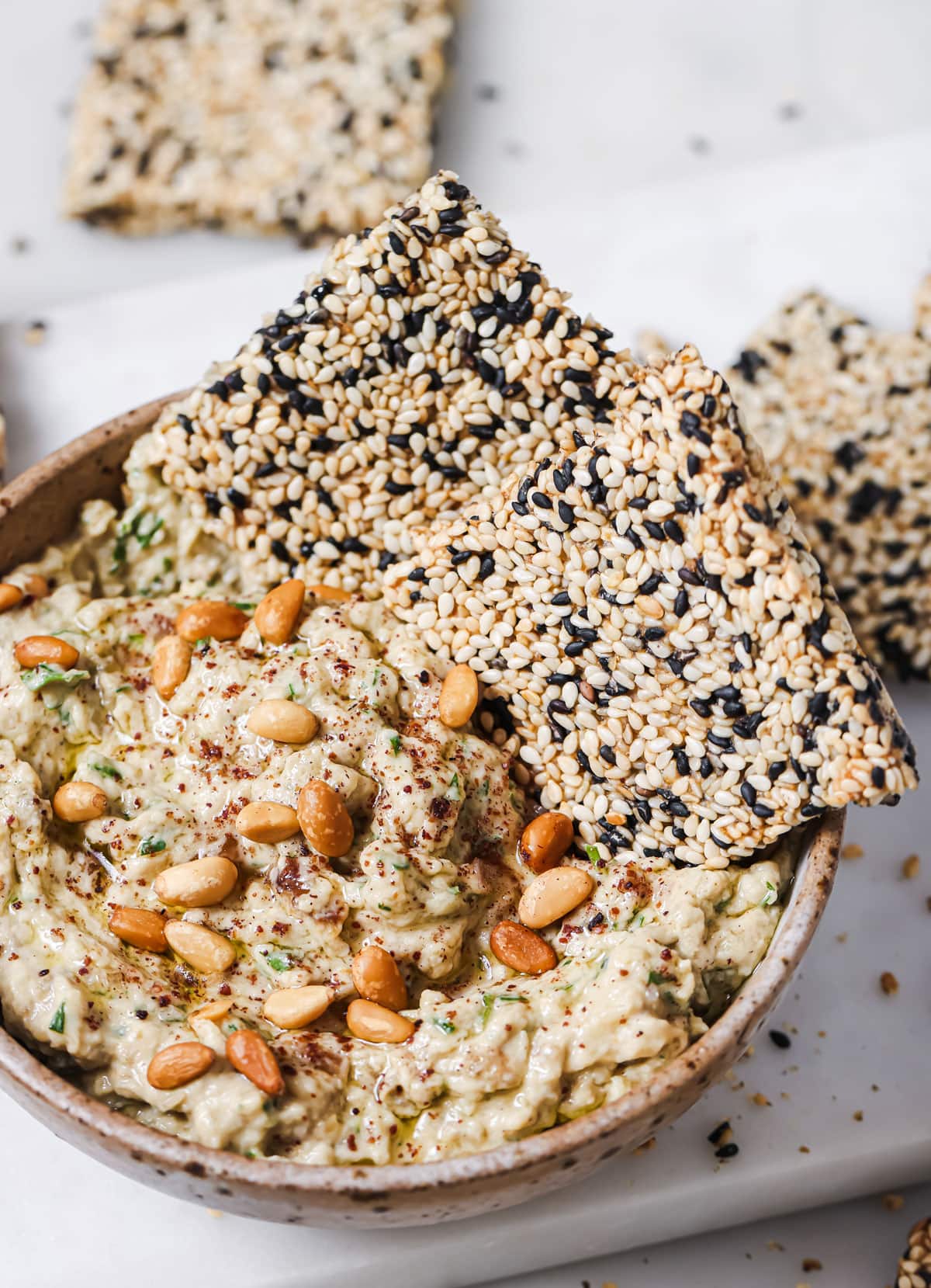 Sesame seed crackers dipped in a bowl with baba ghanoush.