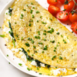 A folded omelette filled with spinach and feta on a plate topped with chopped chives.