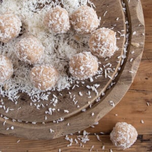 Tahini bliss balls coated in desiccated coconut on a wooden board.