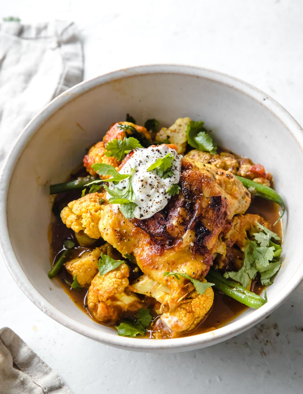 A serving bowl with chicken and cauliflower curry topped with a dollop of yogurt.