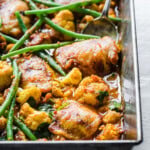 Chicken cauliflower curry topped with green beans in a casserole and a spoon.