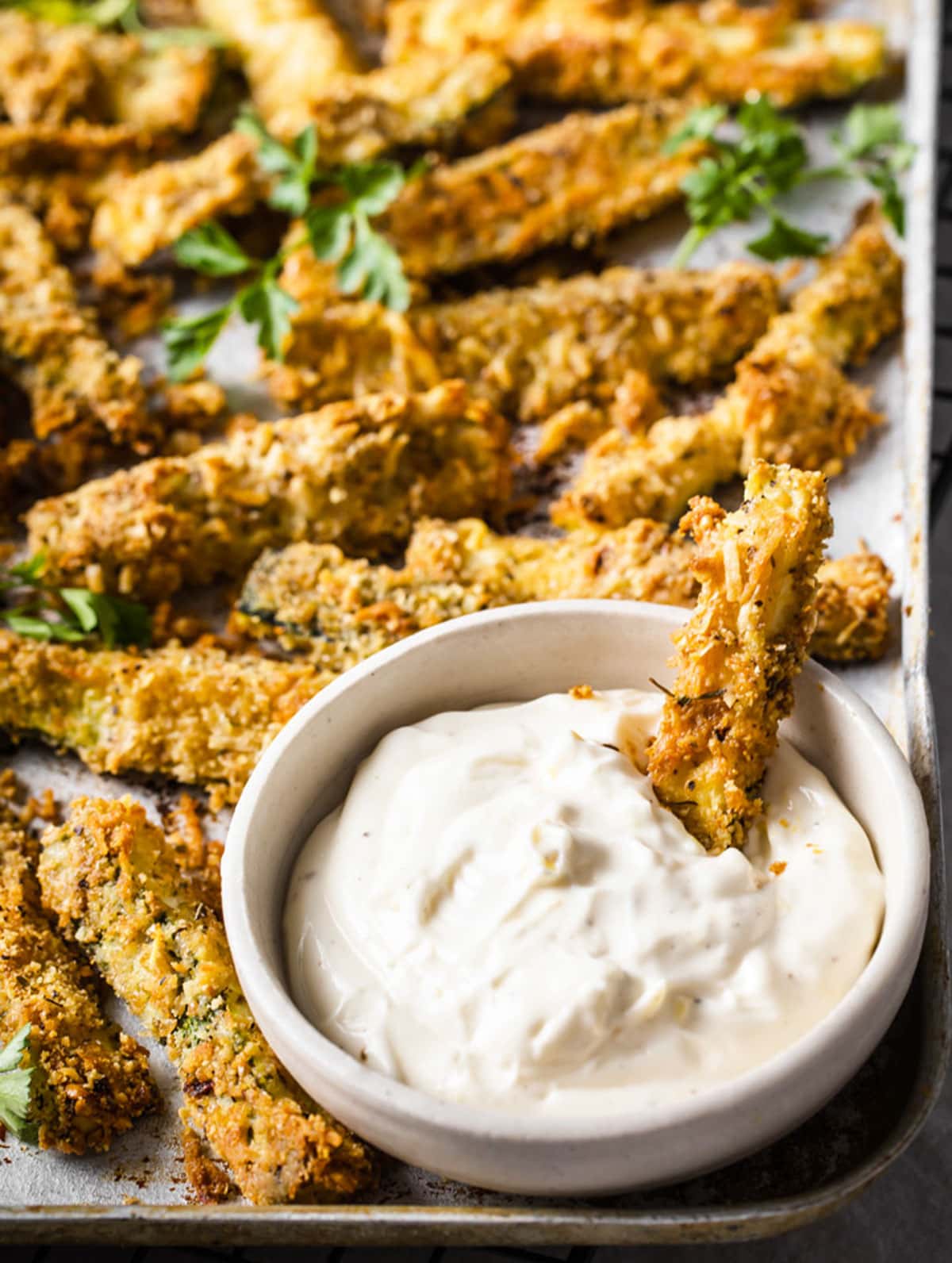 Zucchini fries on a baking sheet and a zucchini in a bowl with lemon aioli.